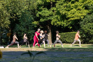 Dişi bir yoga ustası yoga eğitimini dışarıda yürütür ve egzersizleri doğru yapmaya yardımcı olur.