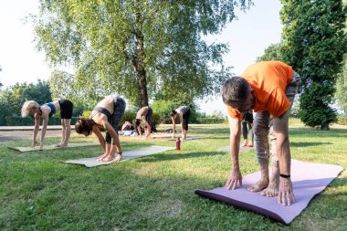 İnsanlar spor minderinin üzerinde durup grup yogası yapıyor.