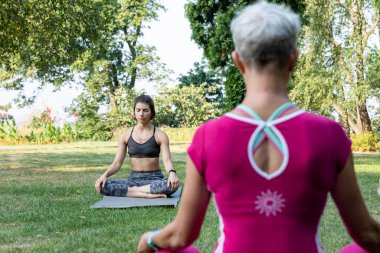 Lotus pozisyonunda oturan kadın çimlerin üzerinde ve zen ustasının arka planında dinleniyor.