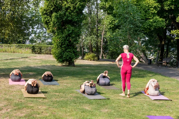 Kadın yoga ustası gruba kasları germek için dizlerinin üzerine çöküp poz vermelerine yardım ediyor.