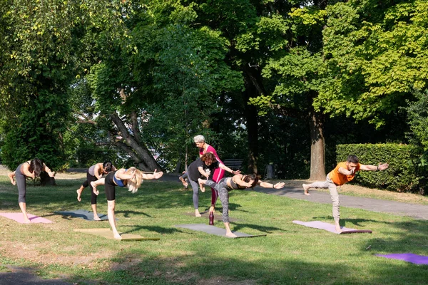 Yoga pozu. Dışarıda yoga sporları yapan bir grup insan, Savaşçı Virabhadrasana pozisyonunda duruyorlar.