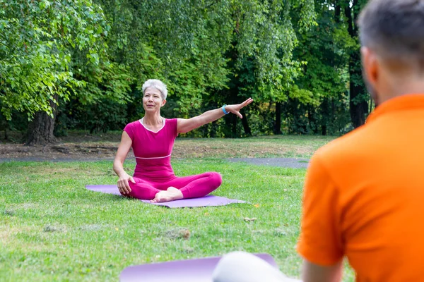 Bayan yoga öğretmeni parkta öğrencileriyle lotus poz veriyor.