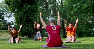 Spor yapan bir grup insan çimlerin üzerindeki bir yoga ustası için kollarını uzatıyorlar.