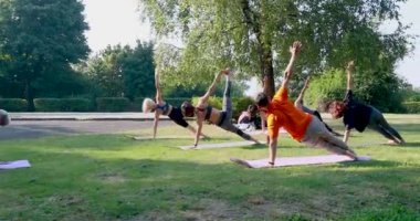 Kamera kaydı, bir grup insanın yoga çalışmasını ve çimlerin üzerinde bir kadın yoga ustasının yan plank pozunu tekrarlamasını gösteriyor.