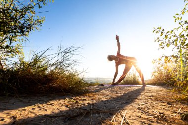 Gün doğmadan önce çimenlerin üzerinde egzersiz yapan bir kadının silueti.