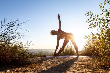 Zen yogasının kadın ustası bir tepede duruyor ve üçgen şeklinde egzersiz yapıyor.