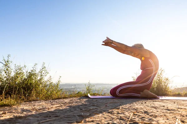 Güneş ışınları dizlerinin üzerinde oturan ve kollarını yoga pozisyonunda ileri doğru uzatan bir kadının üzerinde parlıyor.