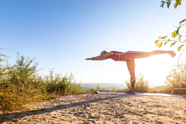 Güneş doğarken çimenlerde yoga yapan bir kadın.