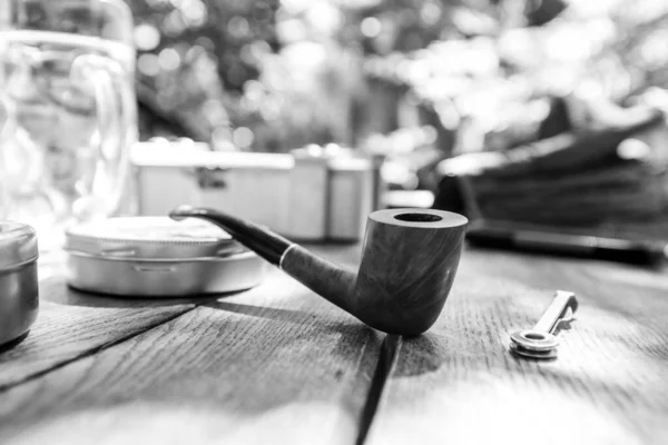 Black and white photo tobacco pipe on the table near a glass of beer and a box of tobacco