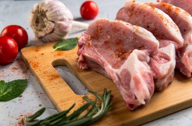 Pork chop sarımsak, domates, bir kesme tahtası üzerinde otlar ile yemek pişirmek için kemik üzerinde.