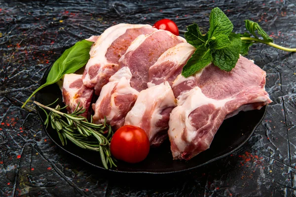 Pork chop sarımsak, domates, bir kesme tahtası üzerinde otlar ile yemek pişirmek için kemik üzerinde.
