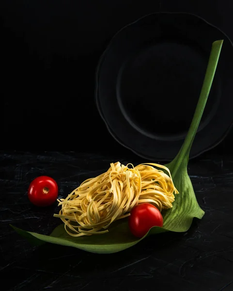 Ham İtalyan makarna Fettuccine yeşil stilize bir tabakta domates ile karanlık bir arka plan üzerinde bırakır.