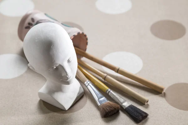 plaster bust for study, which has a ceramic pot with four paint brushes next to it