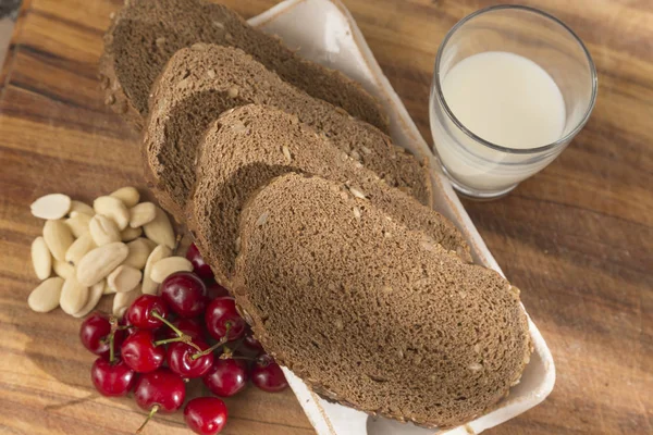 slices of wholemeal bread with pips, cherries, almonds and a glass of milk, healthy and rural breakfast