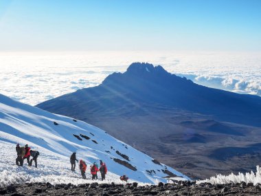 Bulutların üzerinde şafak sökerken, kili ve meru dağları Tanzanya Serengiti 'sinde. Yürüyüşçüler Afrika 'nın en yüksek dağının zirvesine doğru yol alıyorlar.