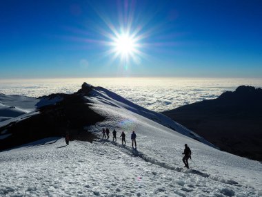 mount kili and meru in the tanzanian serengiti as dawn breaks above the clouds. hikers make their way to the summit of the tallest mountain in africa clipart