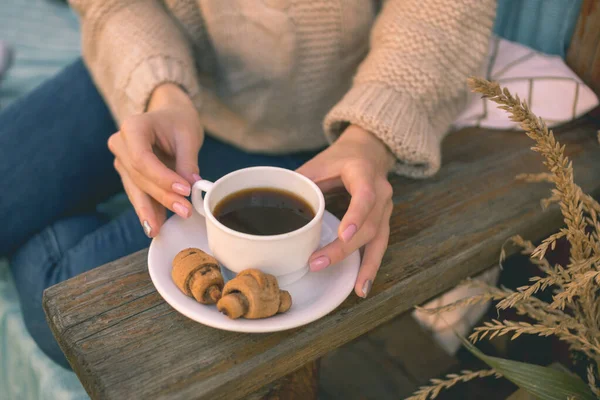 Sonbahar havası. Kahverengi kazaklı ve kot pantolonlu gülümseyen bir kız bankta oturur ve kruvasanla kahve içer.