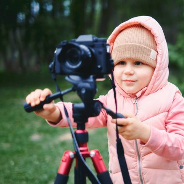 Şehir parkında fotoğraf makinesi olan bir çocuk. Kız internet için bir video ve fotoğraf çeker, kamera için bir video blogu kaydeder. pembe ceket ve şapka