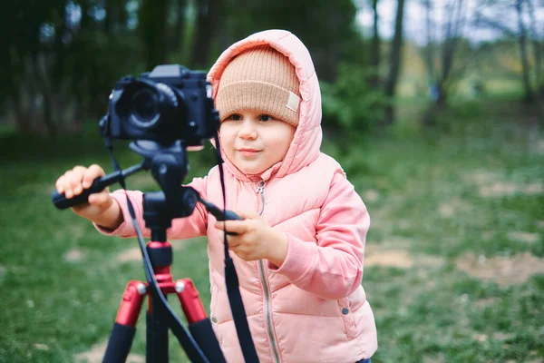 Gyerek fényképezőgéppel egy városi parkban. A lány készít egy videót és egy fotót az internetre, felvesz egy videó blogot a kamerának. rózsaszín kabát és kalap — Stock Fotó