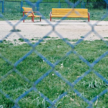 Mavi parmaklıkların arkasındaki boş sarı banklar. Parktaki oyun parkı. Yalıtım. Koronovirüs. Yalnızlık kavramı