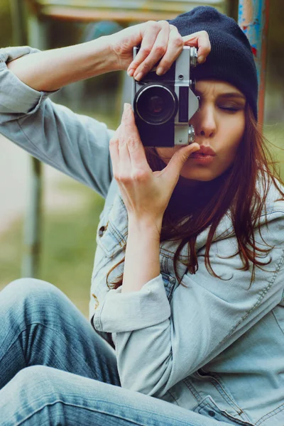 Portré egy gyönyörű hipszter lányról sapkában és farmerdzsekiben fényképezőgéppel Stock Kép