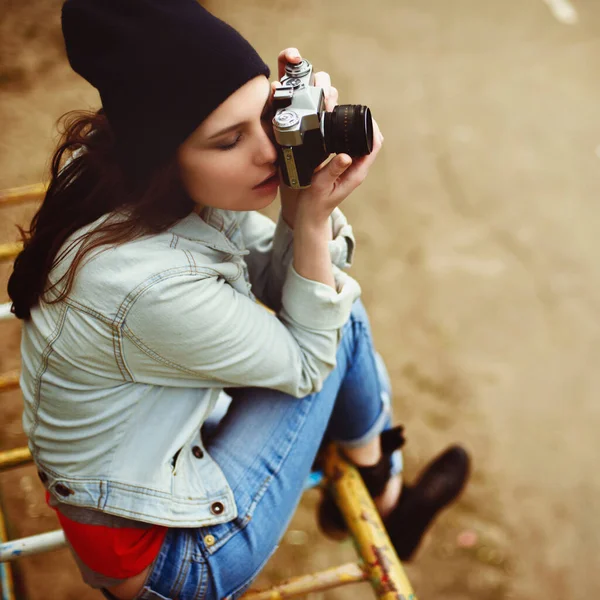 Elinde fotoğraf makinesi olan güzel bir hippi kızın portresi. Parktaki bir çocuk kaydırağında oturuyor. — Stok fotoğraf