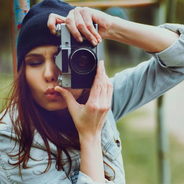 Portret pięknej hipsterki w czapce i dżinsowej kurtce z aparatem fotograficznym robiącym zdjęcia — Zdjęcie stockowe