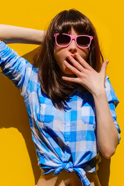 Portret pięknej zaskoczonej dziewczyny w niebieskiej koszuli i okularach na tle pomarańczowej ściany — Zdjęcie stockowe