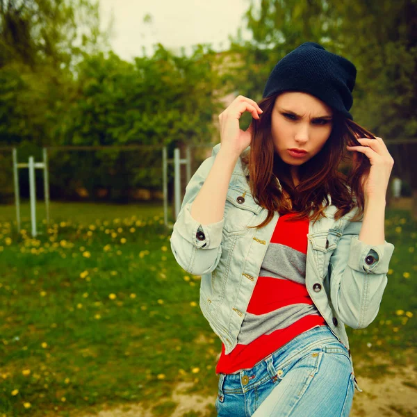 Portrait of a hipster girl in a denim jacket and striped shirt in a park — Stock Photo, Image