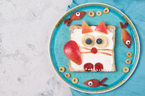 Toast with cream cheese and fruits in a shape of cat, food for kids idea, top view