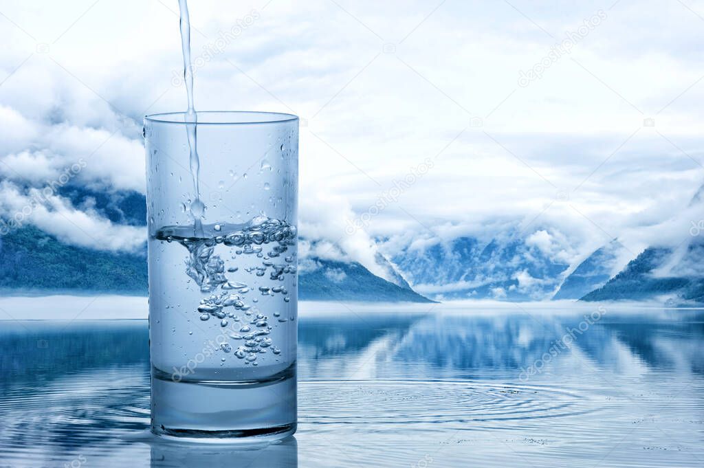 Pouring water into a glass against the nature landscape with lake and mountains