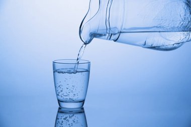 Bir sürahiden mavi arka plandaki bir bardağa su dökülüyor.