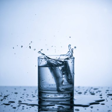 Su bardağına buz küpünden su sıçrıyor.