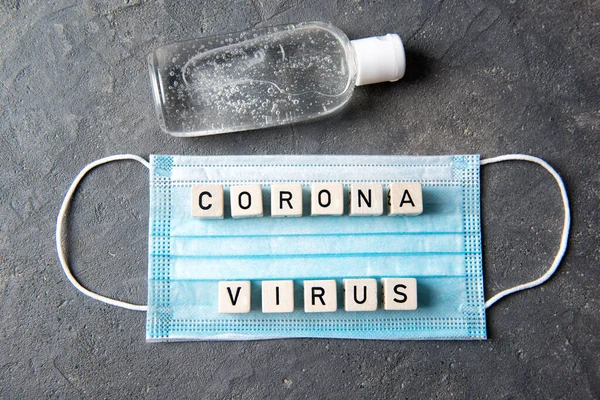 Blue face mask with letters corona virus and bottle with hands disinfectant, top view, health concept