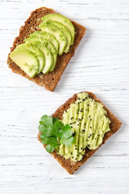 Dilimlenmiş avokado, bahçe teresi filizi, püre avokado ve susam tohumlu ekmek, susam tohumu ve maydanoz, sağlıklı beslenme konsepti, üst görüş.
