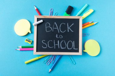 Okul karatahtası ile okul metni ve çeşitli kırtasiye aksesuarları, okul konsepti, üst görünüm, mavi arkaplan