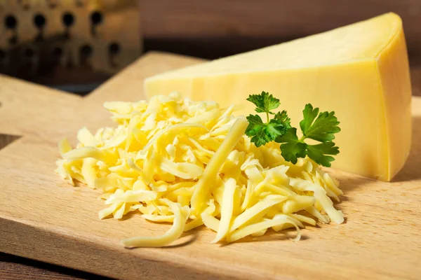 Grated cheese and cheese triangle on wooden cutting board