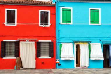 Burano, Venedik, İtalya 'daki parlak kırmızı ve turkuaz evlerin önünde.