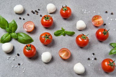 Fesleğen yapraklı taze kiraz domatesleri, mini mozzarella ve taş bir masada kara biber, sebze desenli.