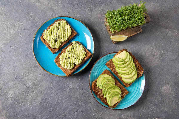 Avocado toasts on whole grain bread, sliced and mashed avocado with garden cress sprouts and lime, healthy eating concept, top view