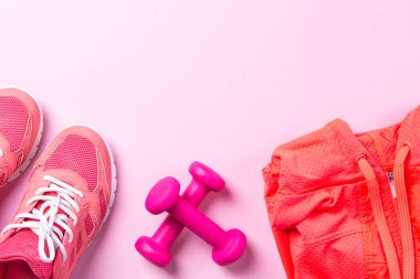 Fitness konsepti, pembe spor ayakkabılar, pembe arka planda spor gömlekli dambıllar, fotokopi alanı olan üst manzara.