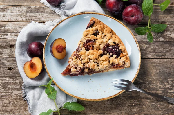 Piece of Plum Cake on a plate with ripe plums and mint leaves, wooden table