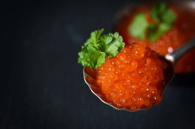 Kırmızı havyar gümüş kaşıkla süslenmiş koyu bir arka planda, seçici bir odak noktası var.