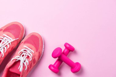 Fitness konsepti, pembe spor ayakkabıları ve pembe arka planda dambıllar, fotokopi alanı olan üst manzara.
