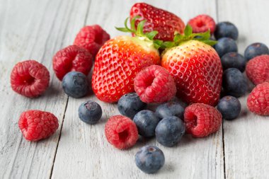 Gri ahşap arka planda taze meyve, çilek, yabanmersini ve ahududu.