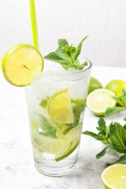 Taze limonlu mojito kokteyli ve açık gri taşlı arka planda bir bardakta nane yaprağı.