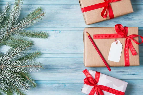 Etiketli ve kalemli Noel hediyesi kutuları, karlı köknar dalı, ahşap arka plan, üst görünüm