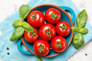 Bir kasede taze kiraz domatesleri, fesleğen yaprakları ve taş masada karabiber, yakın plan, üst görüş.