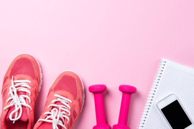 Fitness konsepti, pembe spor ayakkabıları ve pembe arka planda akıllı telefonları olan dambıllar, fotokopi alanı olan üst görünüm.
