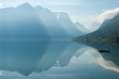 Göle yansıyan dağlarla manzara ve Norveç 'te küçük bir tekne.